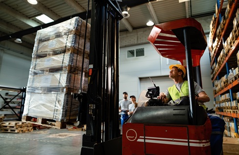 Warehouse worker moving pallets with a forklift in industrial building.